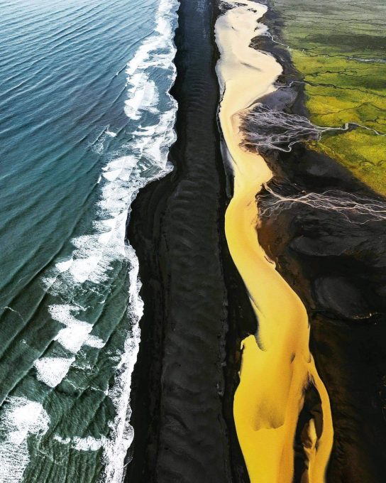 12. There's a place in Iceland where green fields, a yellow river, a black beach and the ocean meet.